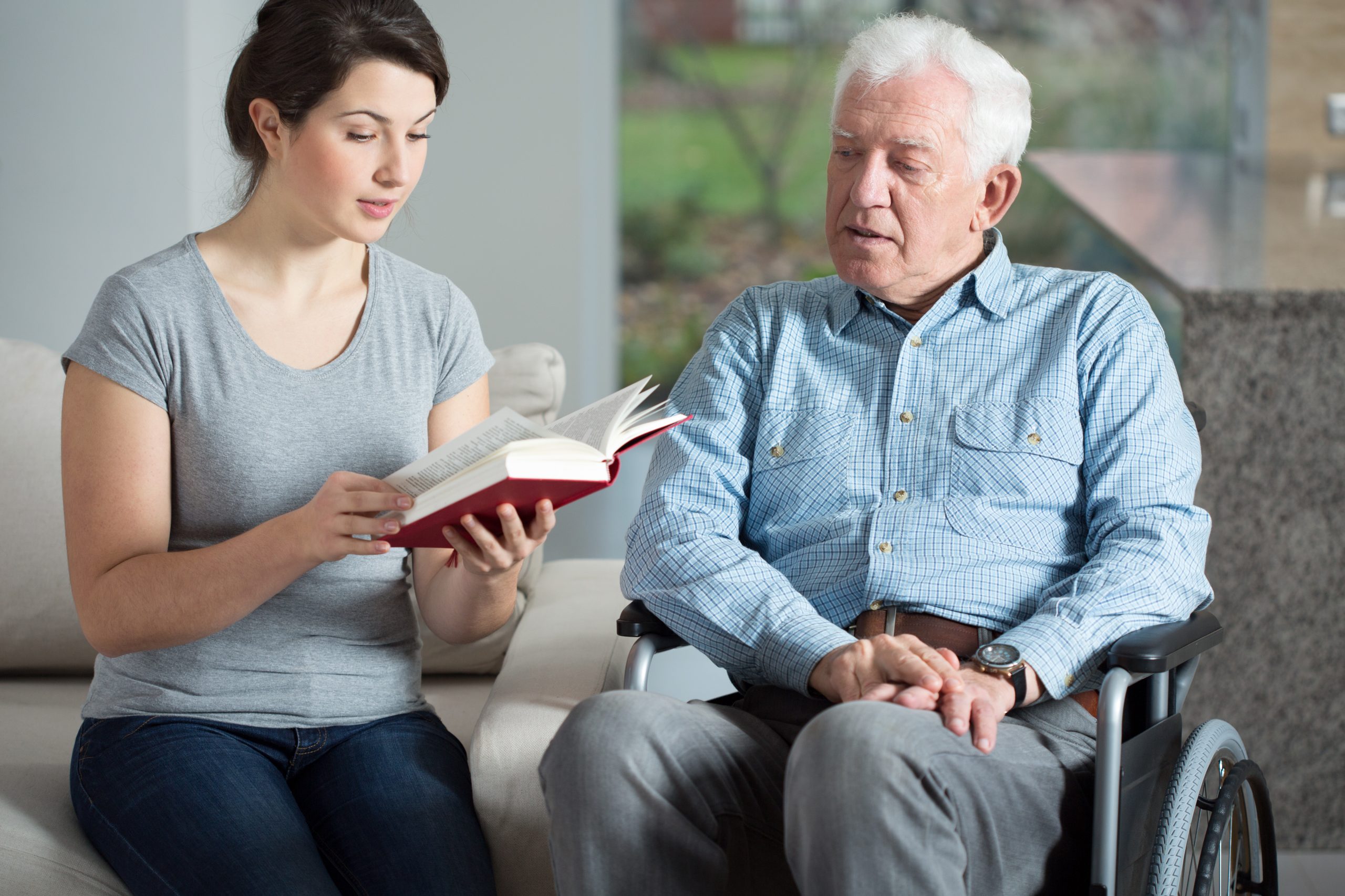 Pflegerin liest älterem Herrn aus einem Buch vor 24 Stunden Betreuung, Pflegerin liest älterem Herrn aus einem Buch vor
